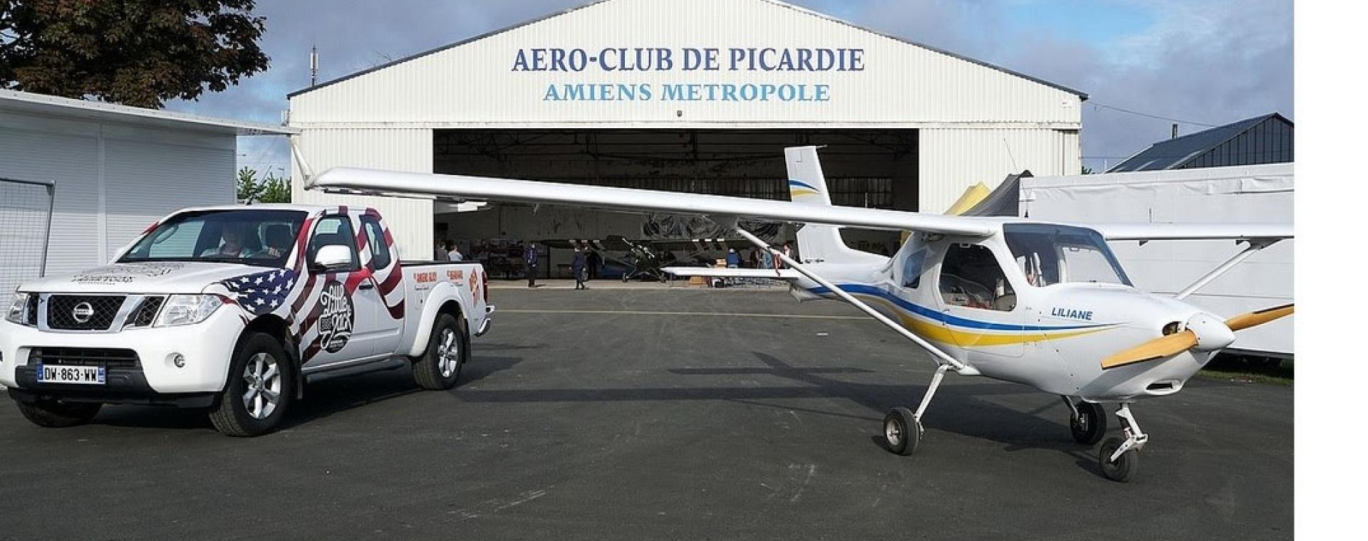 Photo du hangar de l'aéroclub de Picardie à Glisy. Un avion et une voiture sont stationnés en extérieur.